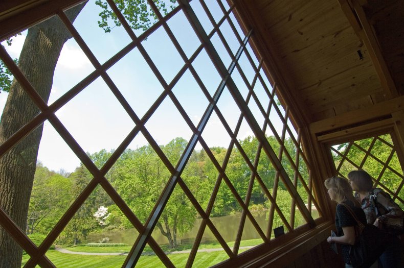 Two people look out a large wooden with a wood lattice out at an area of green grass and trees