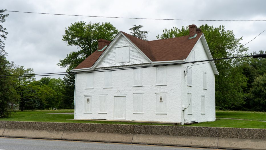 image of a white house with red roof and boarded white windows