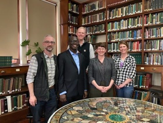 Five adults standing behind a table in a library