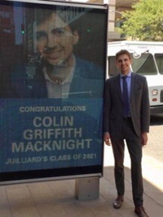 a person standing outside next to a bus shelter with a poster that says "Congratulations"