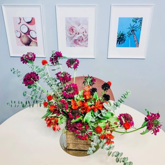 An asymetrical floral arrangement in a gold vase sitting on a white table cloth.