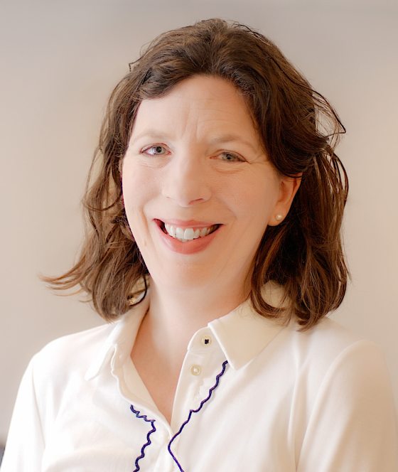 A headshot of a person with medium length brown hair, smiling at the camera.