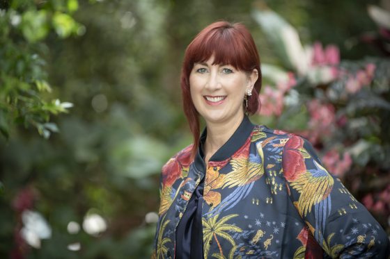 A person in a floral jacket and short reddish hair smiling at the camera.