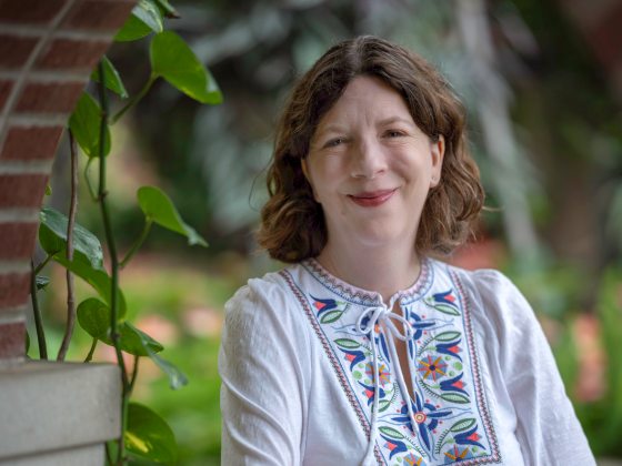 A woman with brown hair in a white shirt with a colorful pattern down the middle smiles.