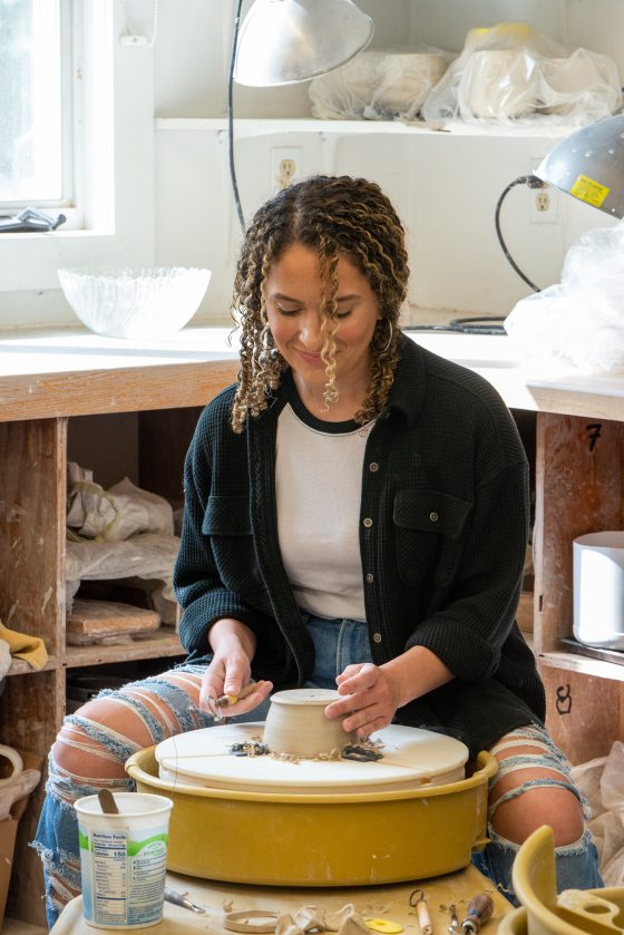 A person sitting at a wheel spinning clay.