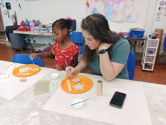 An adult and child painting ceramic pieces at a work table.